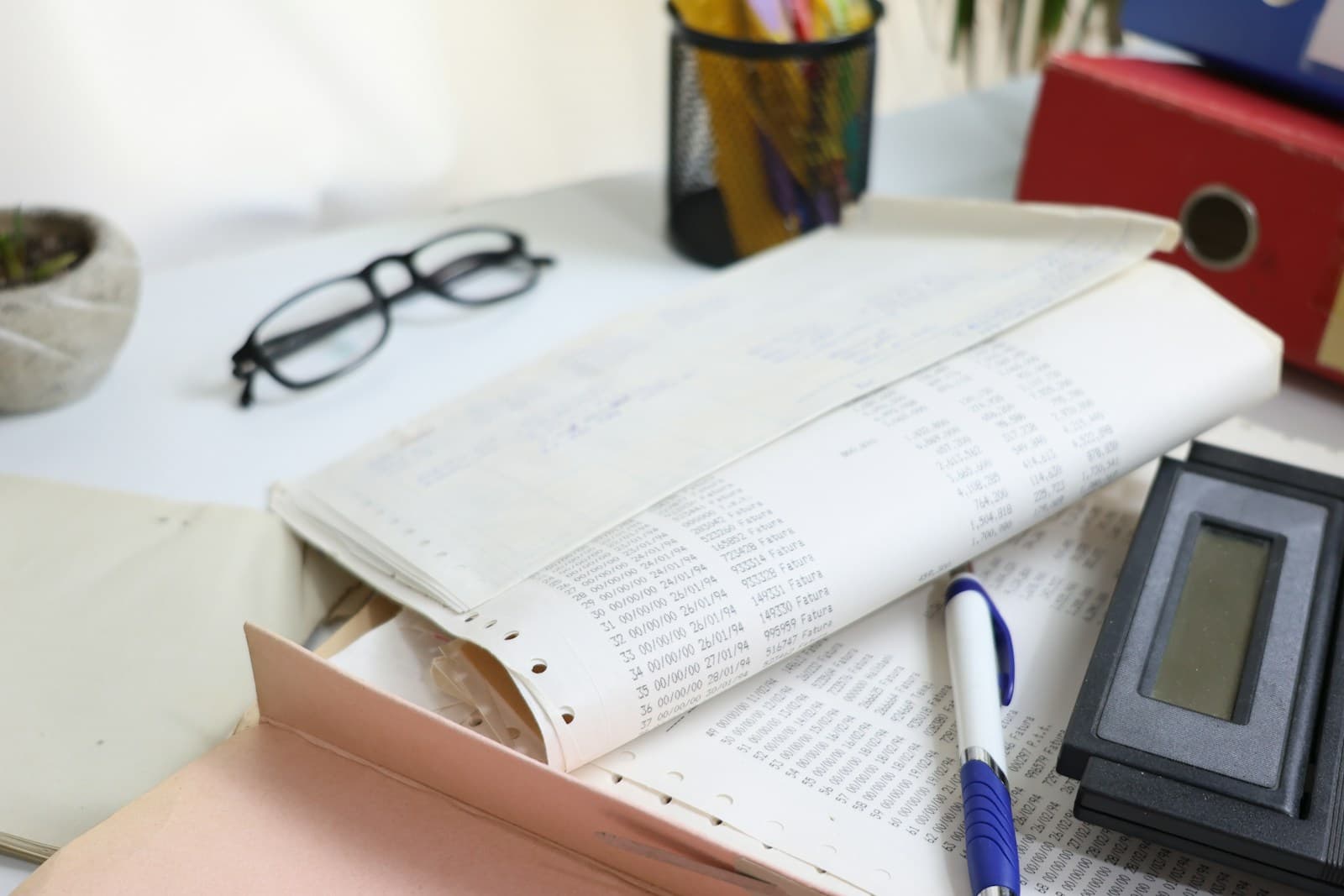 Paper accounts, a calculator, pen and glasses on a desk.